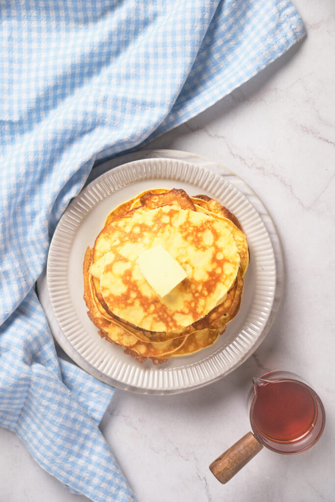 A stack of pancakes with a pat of butter on top, placed on a white plate.