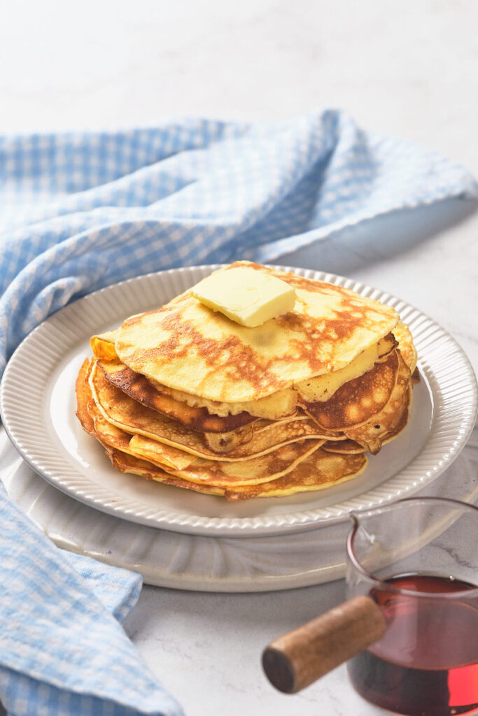 A stack of pancakes topped with a pat of butter on a white plate.