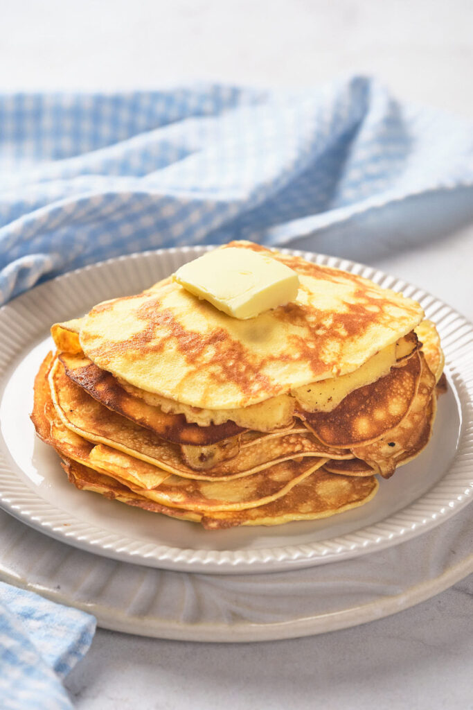 A stack of pancakes with a pat of butter on top sits on a white plate.