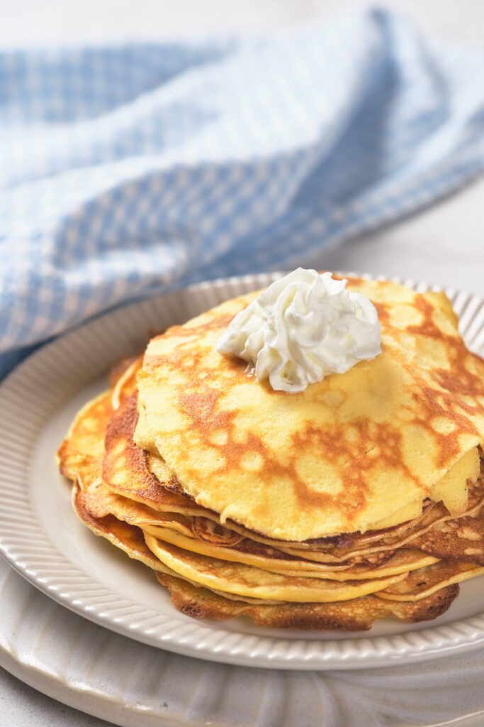 A stack of 2 ingredient pancakes topped with a dollop of whipped cream.