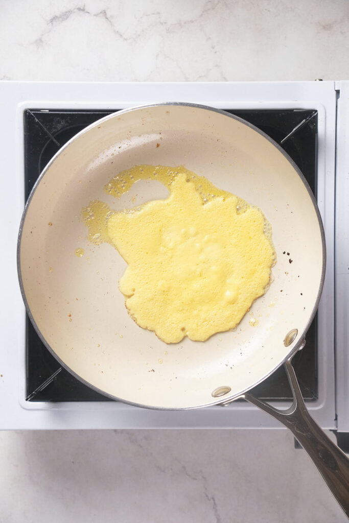 Pancake batter cooking in a non-stick frying pan on a white stove.