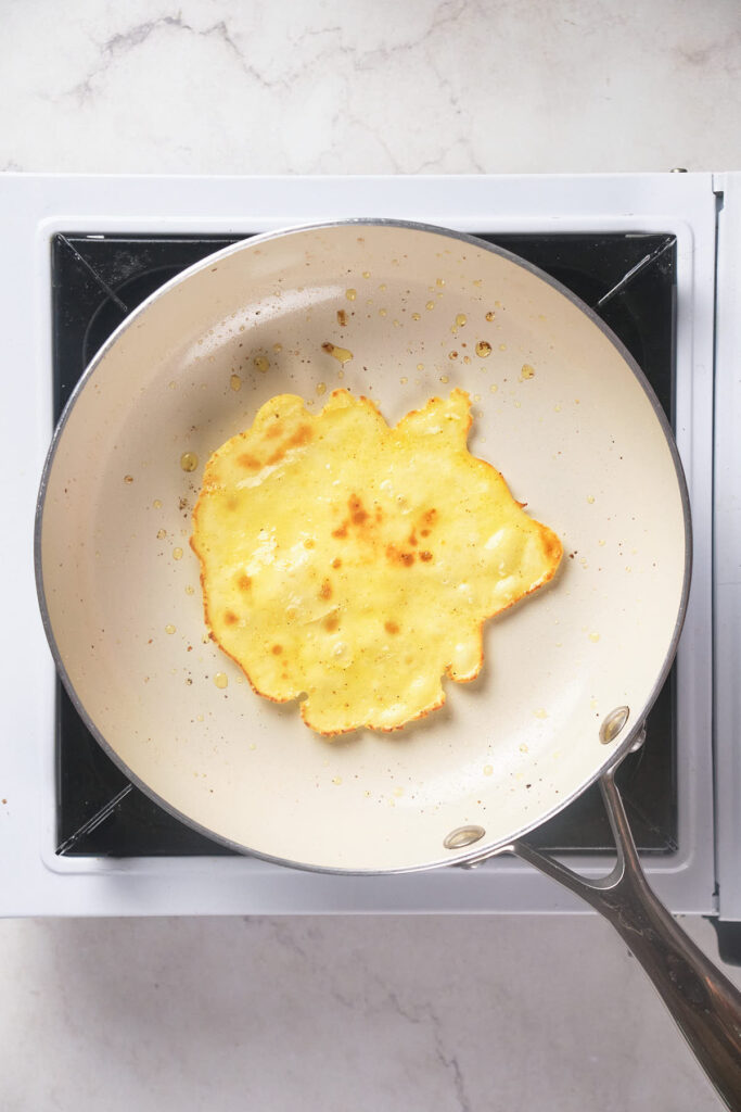 A pancake is being cooked in a white frying pan on a stove.