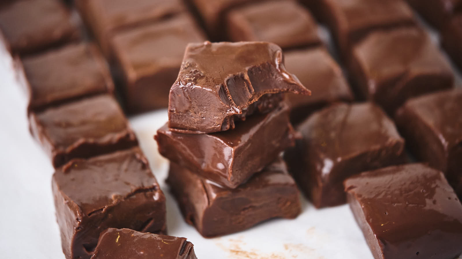 Close-up view of several pieces of chocolate fudge, with some stacked and one showing a bite taken out of it.