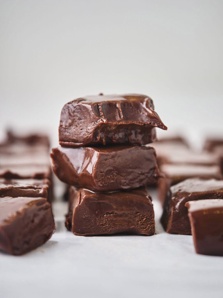 A stack of chocolate fudge pieces on a light surface, with several more pieces arranged in the background.