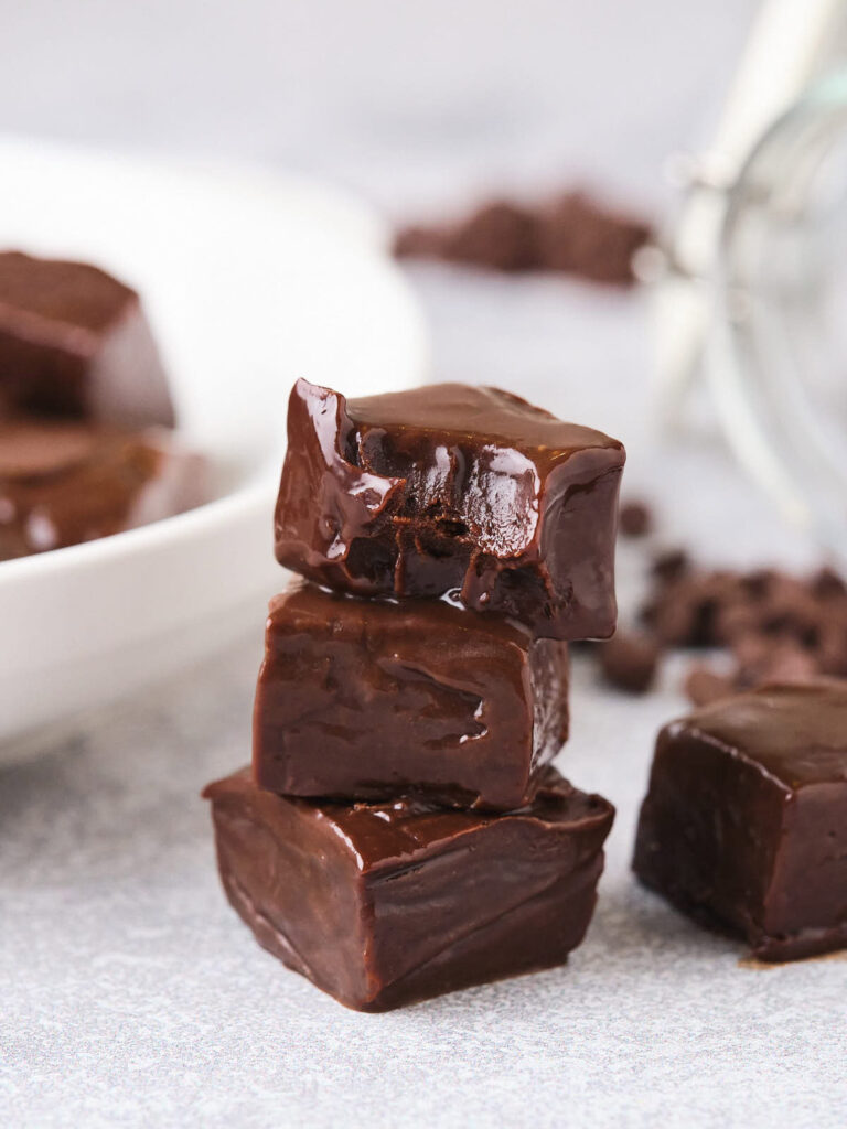 Three pieces of chocolate fudge are stacked on a gray surface.