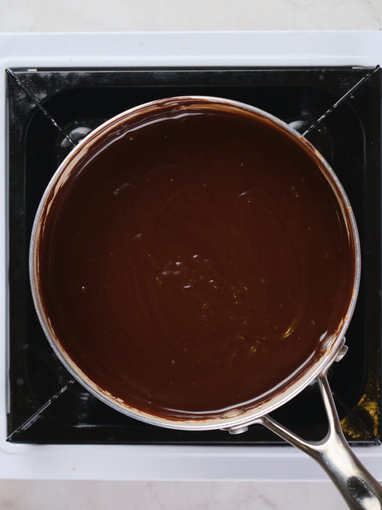 A saucepan filled with melted chocolate placed on a stovetop.