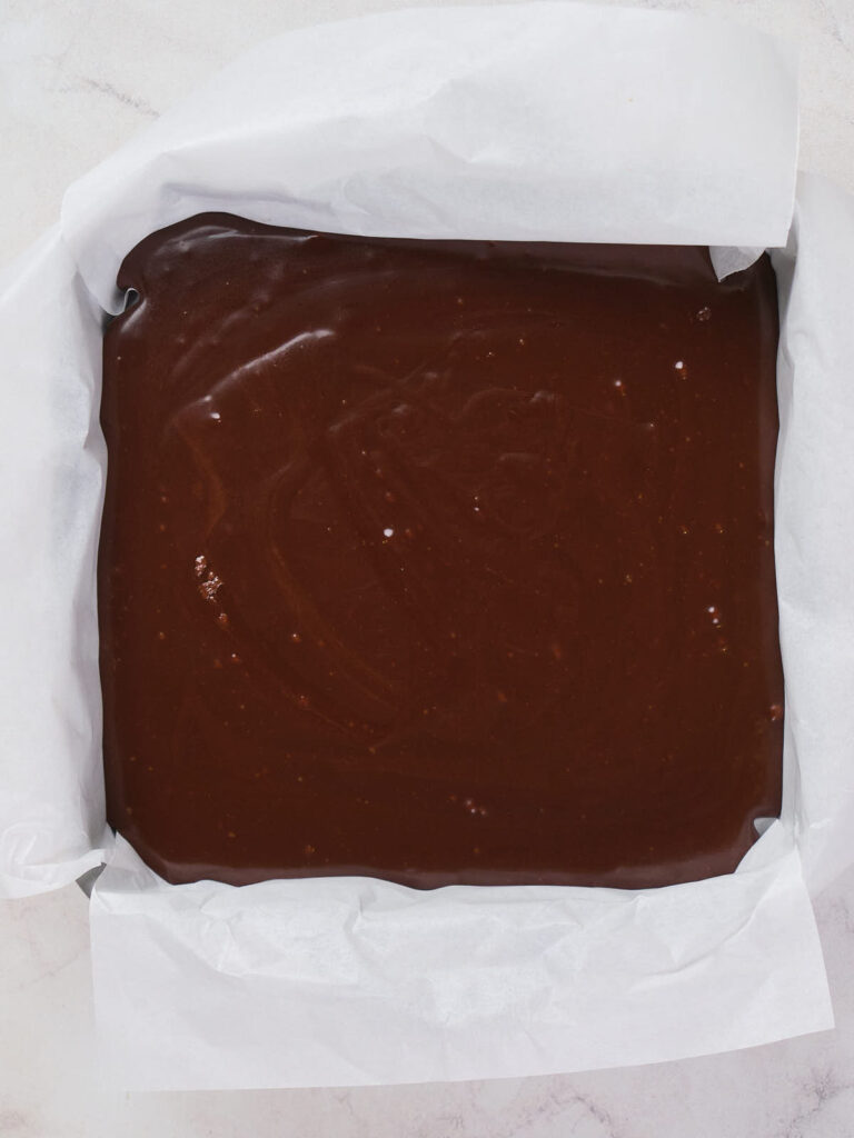 A baking pan lined with parchment paper is filled with smooth, unbaked chocolate batter.