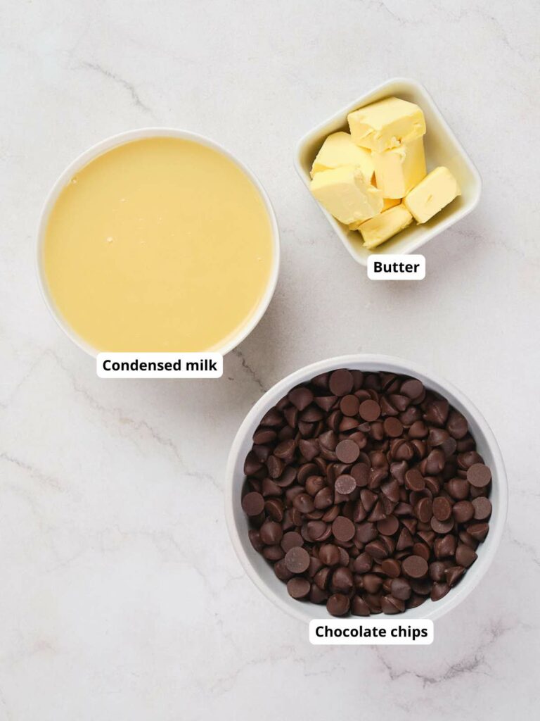 A bowl of condensed milk, a bowl of chocolate chips, and a small bowl of butter cubes.