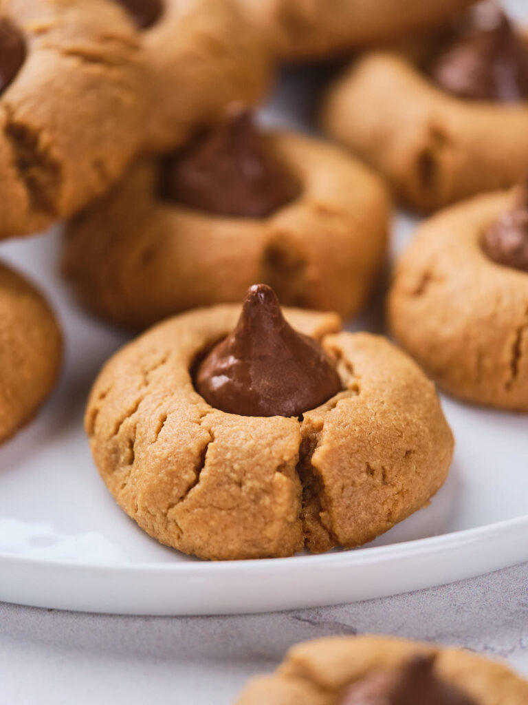 Close-up of peanut butter blossoms with a chocolate drop in the center, displayed on a white plate.