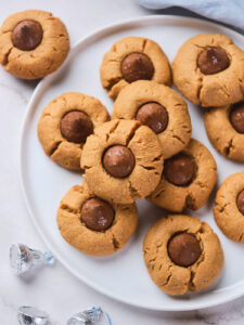 A plate of peanut butter blossoms with chocolate centers arranged on a white plate.