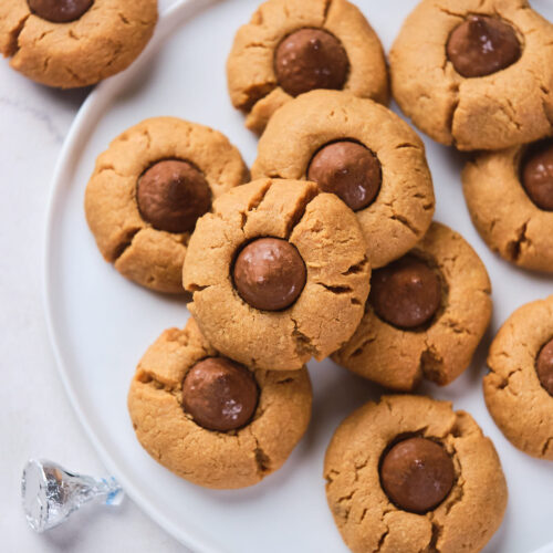 A plate of peanut butter blossoms with chocolate centers arranged on a white plate.