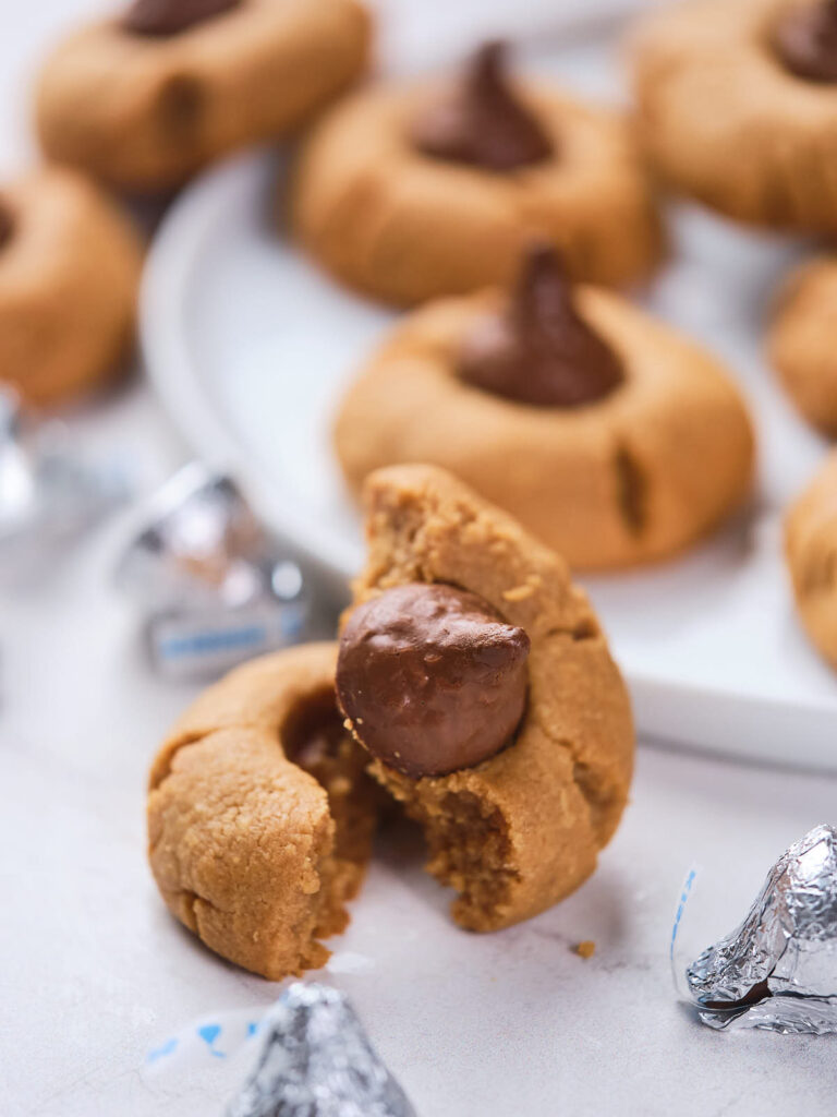 Close-up of peanut butter blossoms, one split in half, topped with chocolate kisses.