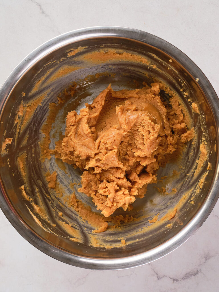 A stainless steel bowl containing peanut butter blossoms dough on a light-colored surface.