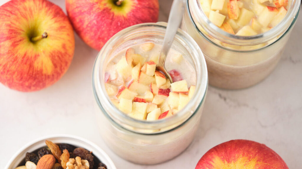 Two jars of apple cinnamon overnight oats on a marble surface.