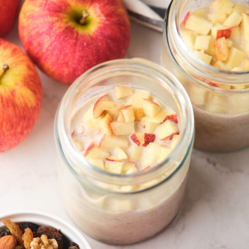 Two jars of oatmeal topped with chopped apples are placed on a table.