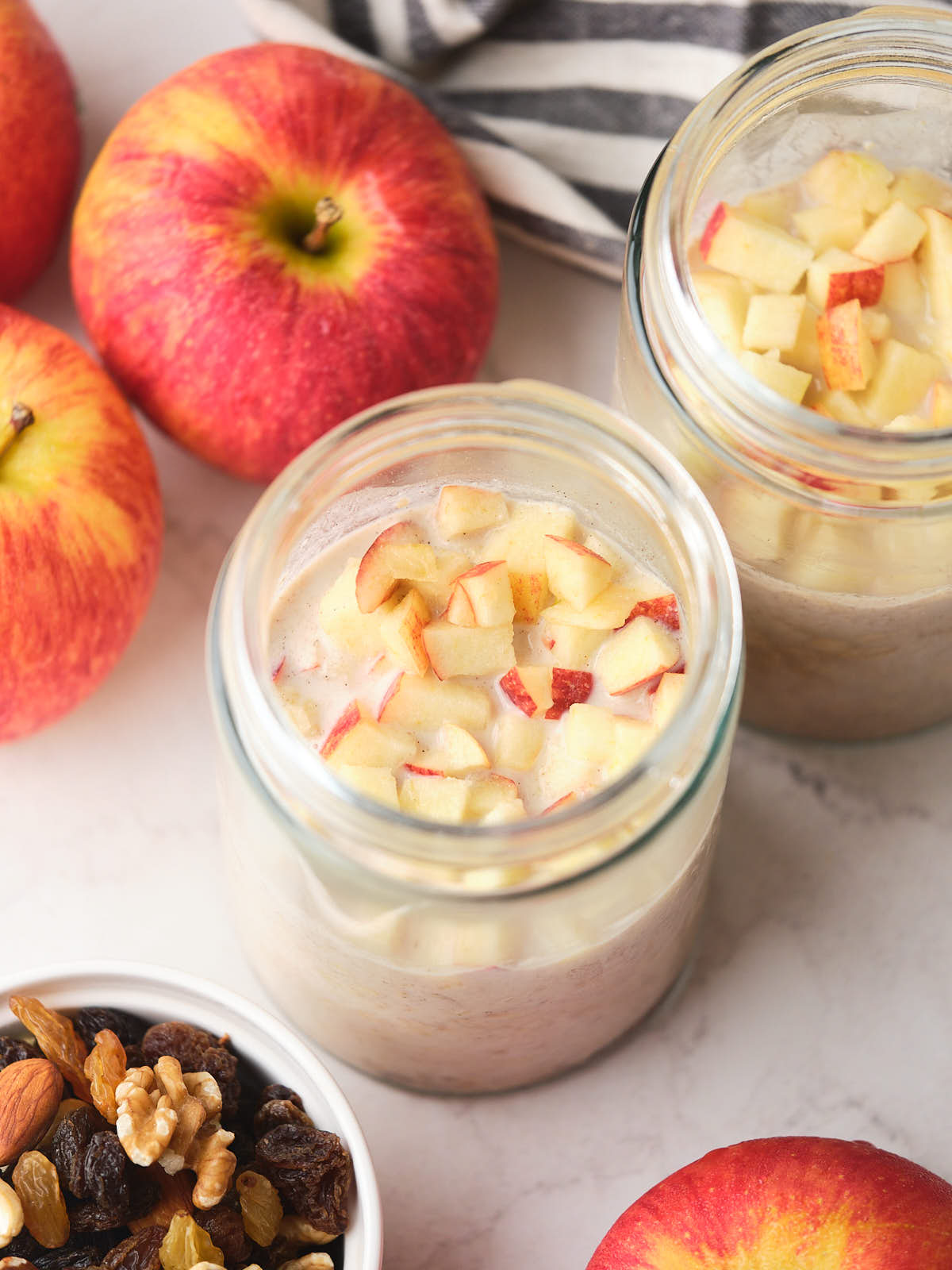 Two jars of oatmeal topped with chopped apples are placed on a table.