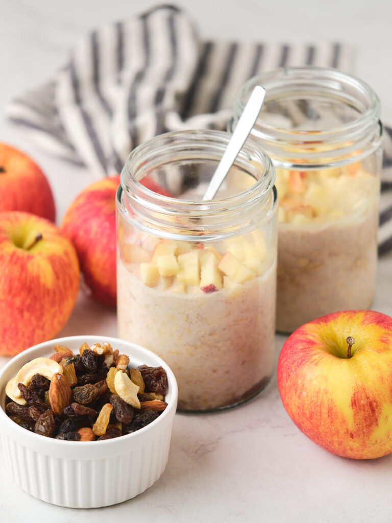 Two glass jars of oatmeal topped with diced apples.