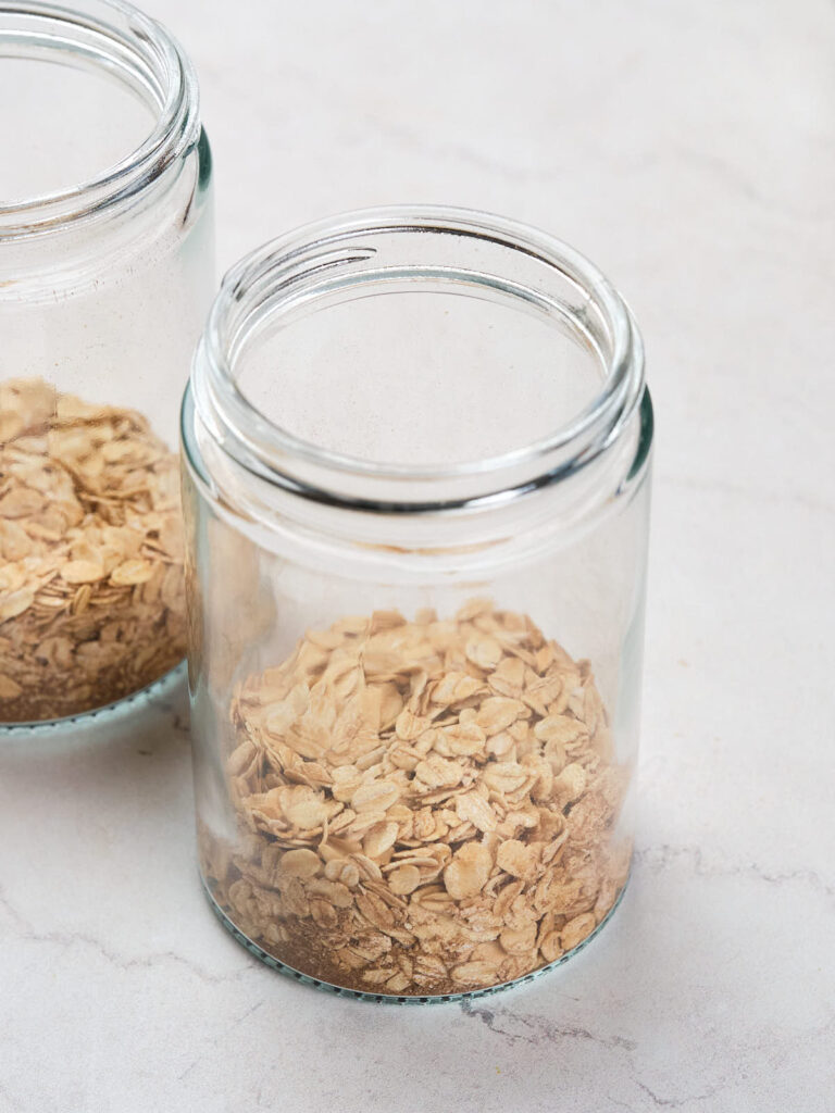 Two glass jars partially filled with rolled oats are placed on a light-colored surface.