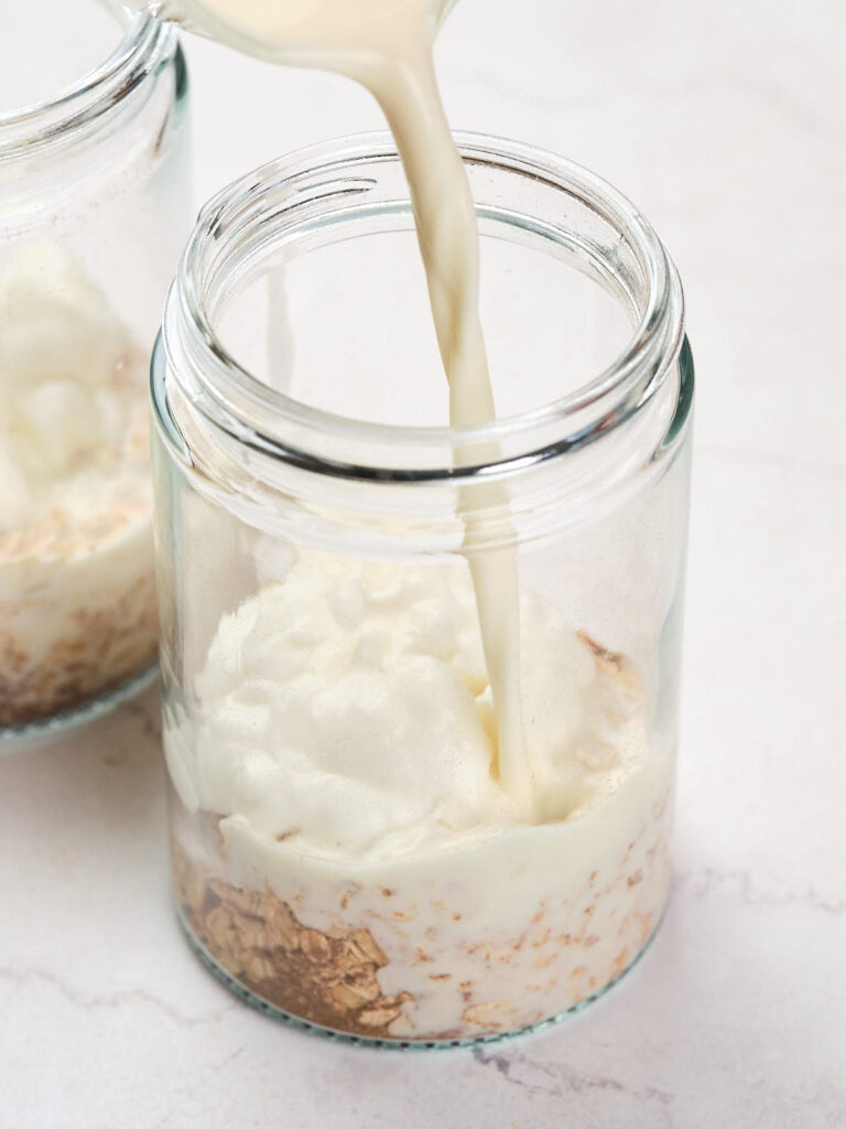 Milk being poured into a glass jar containing yogurt and oats.