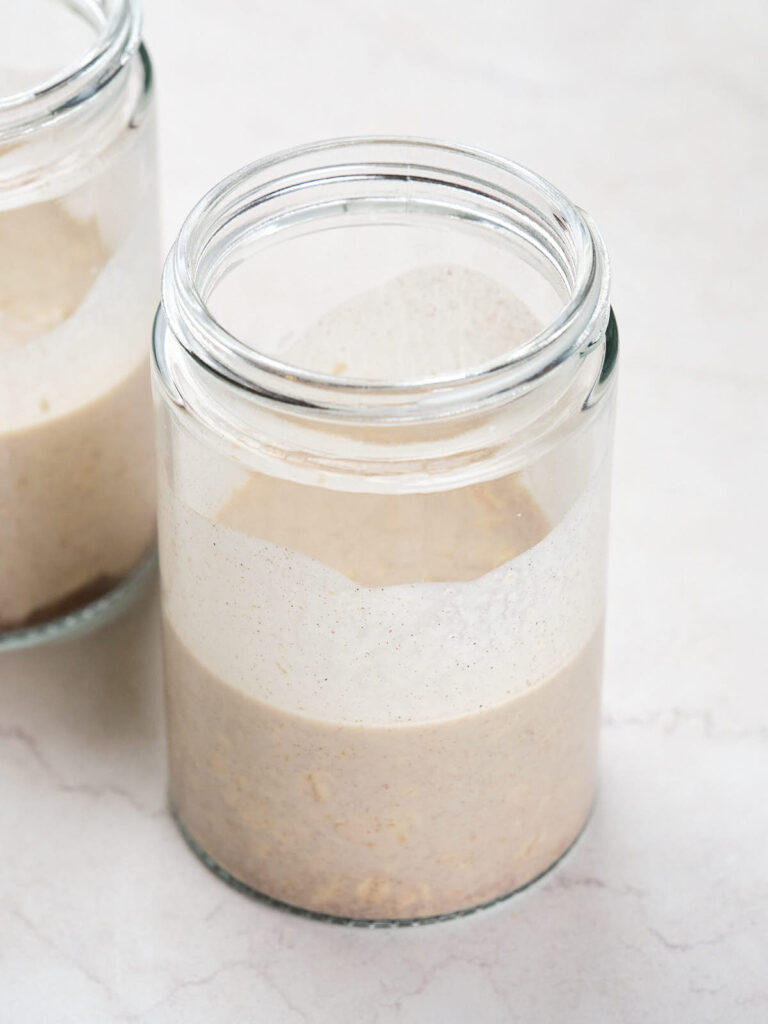 Two clear glass jars on a light-colored surface, each containing a cinnamon overnight oats mixture.