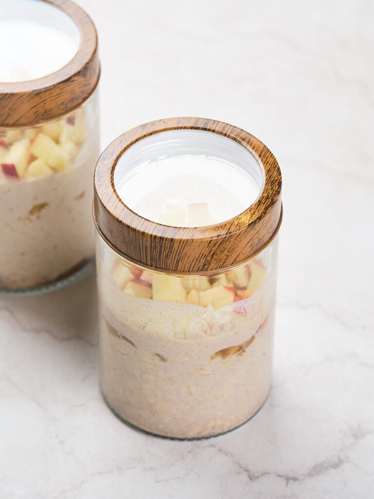 Two glass jars with wooden lids, filled with cinnamon overnight oats mixture.