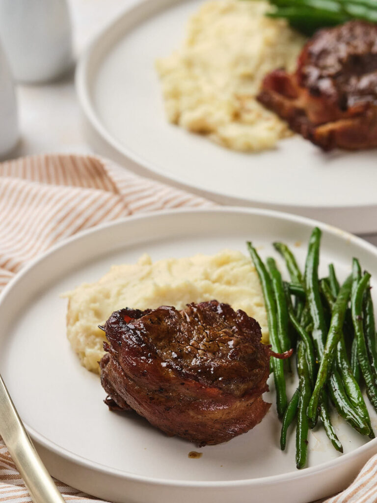 A plated meal featuring a bacon-wrapped fillet mignon.