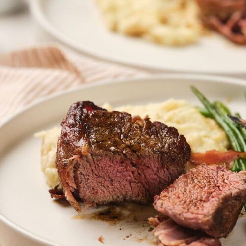 A plate with a piece of cooked bacon-wrapped fillet mignon.