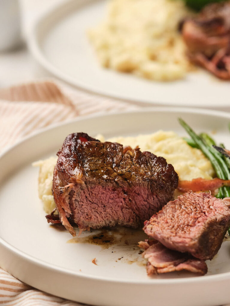 A plate with a piece of cooked bacon-wrapped fillet mignon.