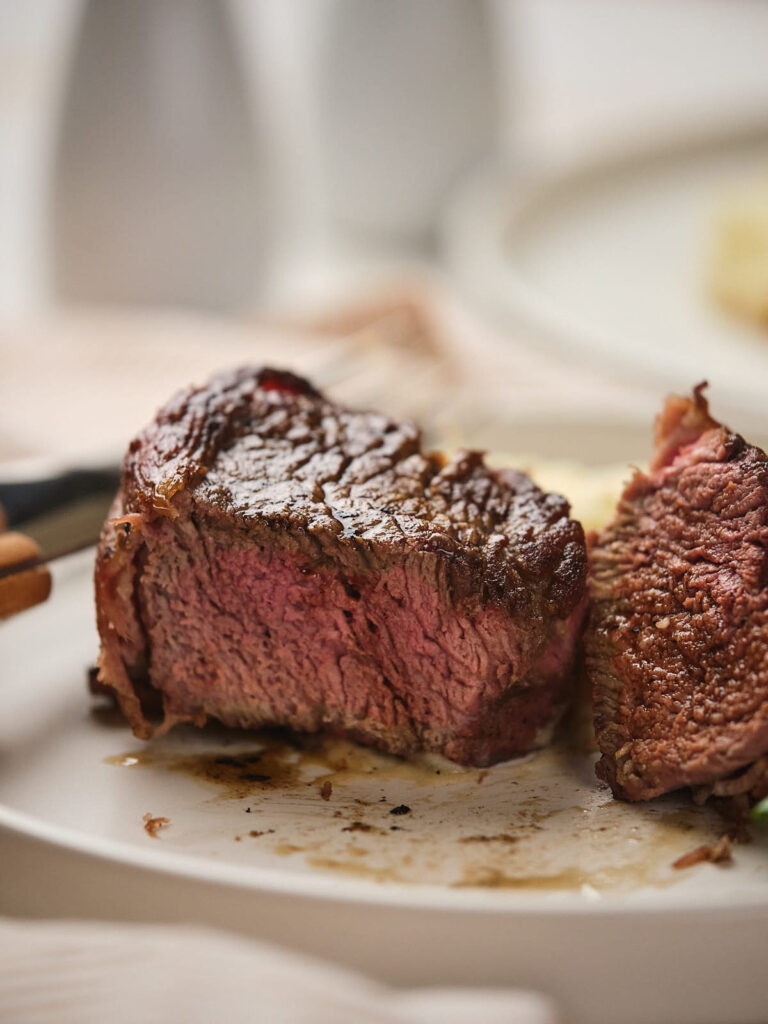 A close-up of bacon wrapped fillet mignon, served on a white plate.