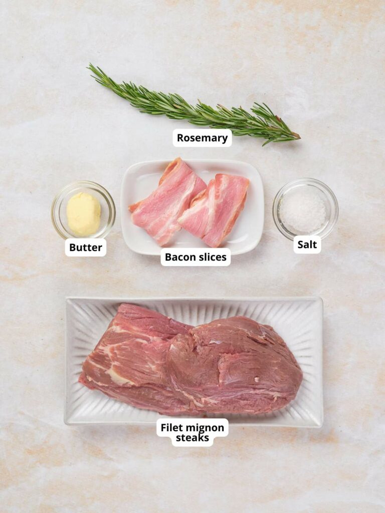 Ingredients for bacon wrapped fillet mignon, each labeled and arranged on a light surface.