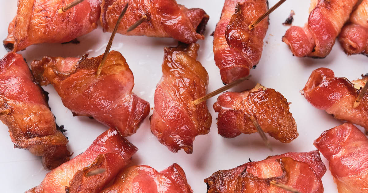 Bacon-wrapped pineapples with toothpicks on a white plate.