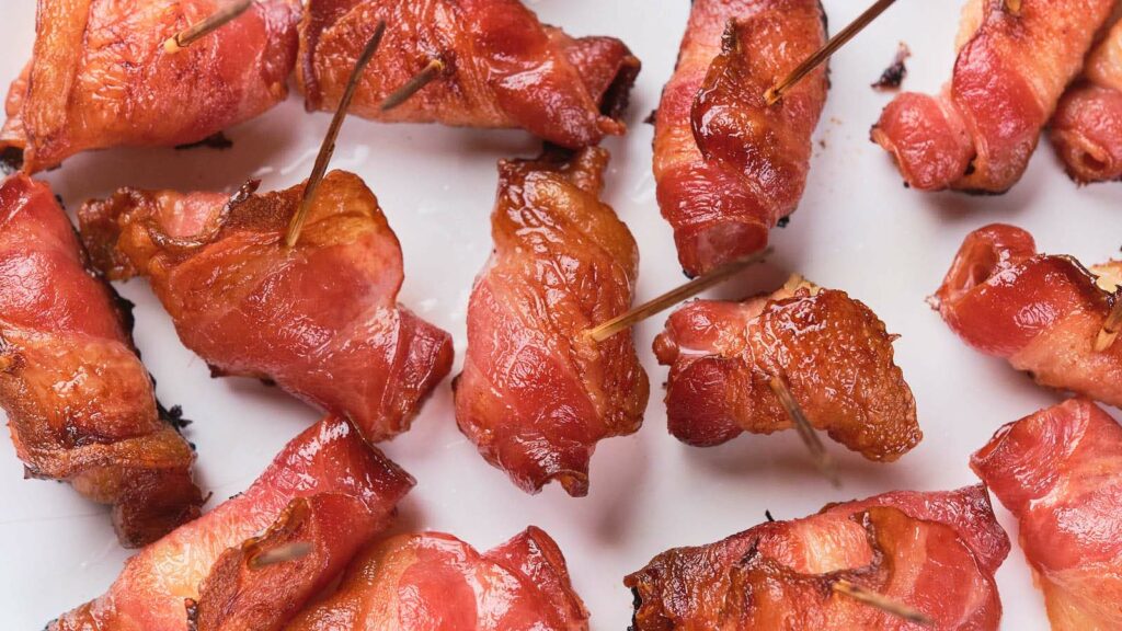 Close-up of bacon wrapped pineapple on a white surface.