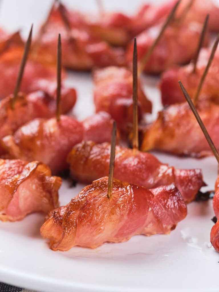 Close-up of a plate featuring bacon-wrapped pineapples, each held together with a toothpick.