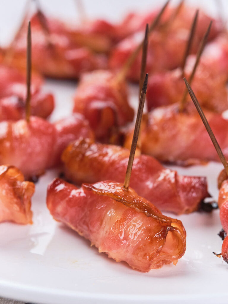 Close-up of bacon-wrapped pineapples secured with toothpicks arranged on a white plate.