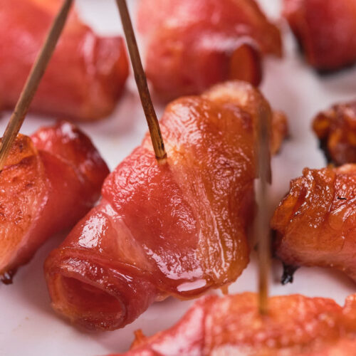 Close-up of bacon-wrapped pineapples secured with toothpicks, arranged on a white surface.