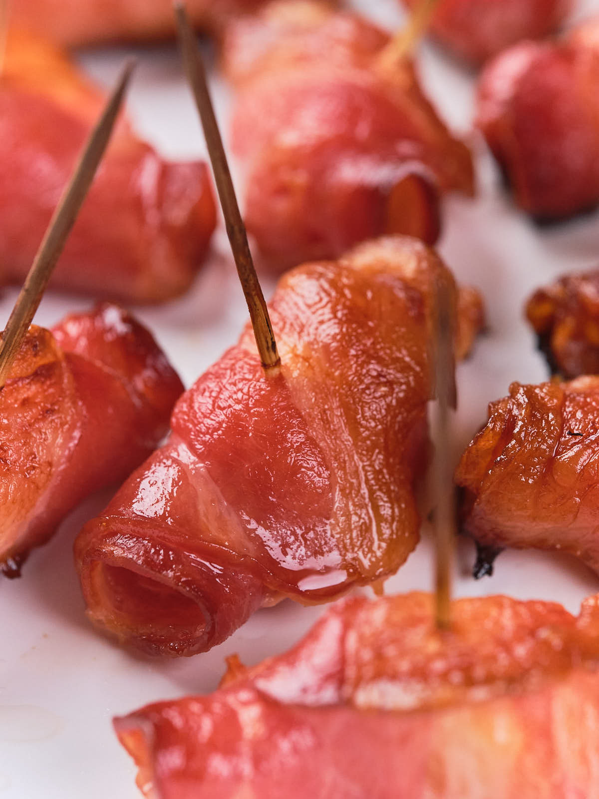 Close-up of bacon-wrapped pineapples secured with toothpicks, arranged on a white surface.