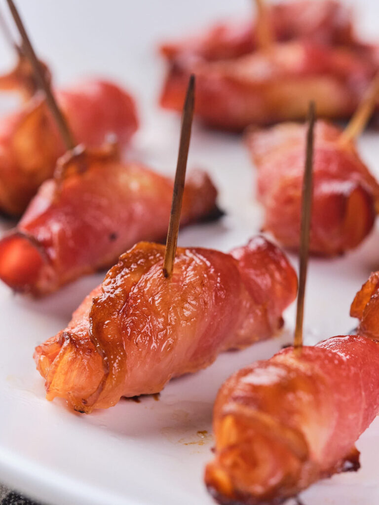 Close-up of bacon-wrapped pineapples on a white plate, each secured with a toothpick.