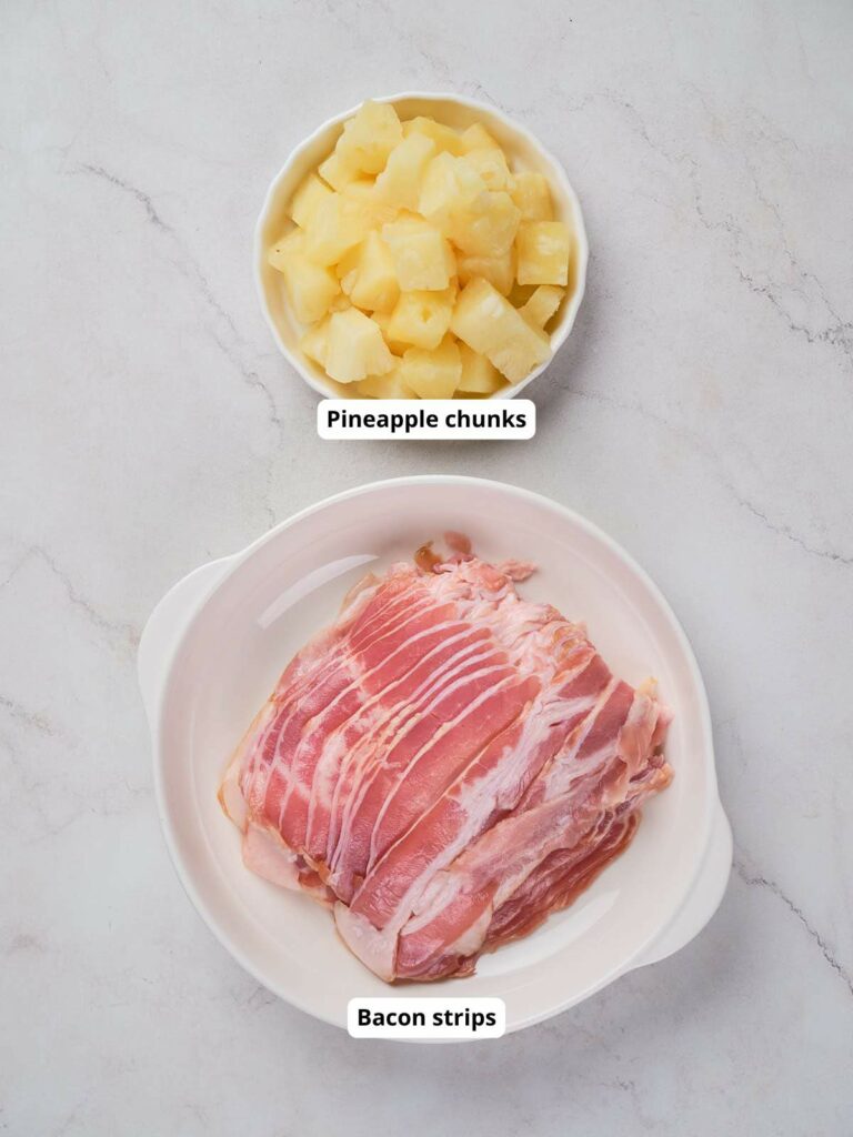 Two bowls on a marble surface: the top bowl contains pineapple chunks, and the bottom bowl contains bacon strips.