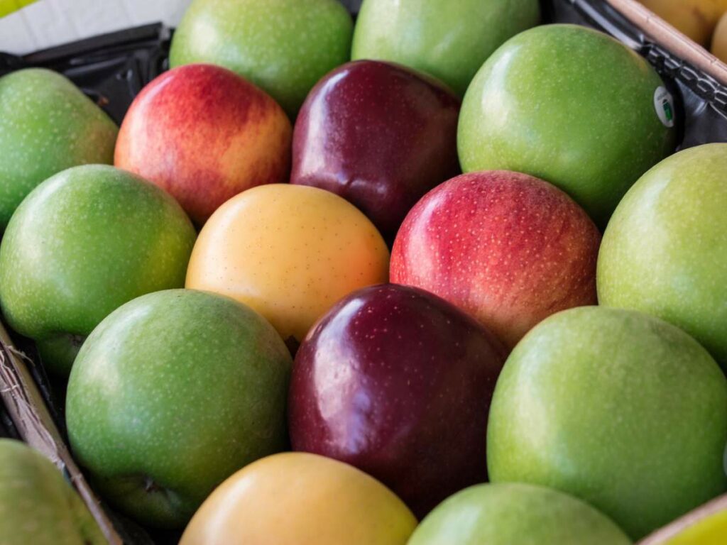 Various apples in a fruit stand with green, red, and yellow varieties closely packed together.