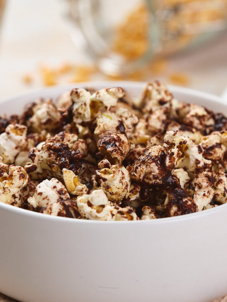 A white bowl filled with popcorn drizzled with melted chocolate.