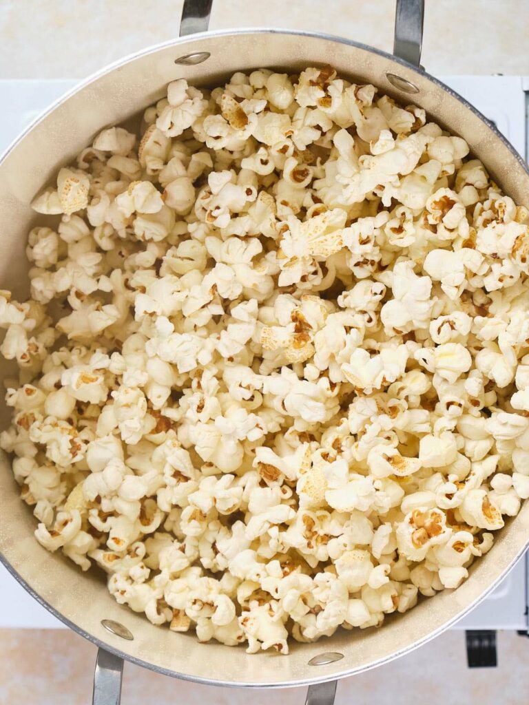 A large metal pot filled with freshly popped popcorn, viewed from above.