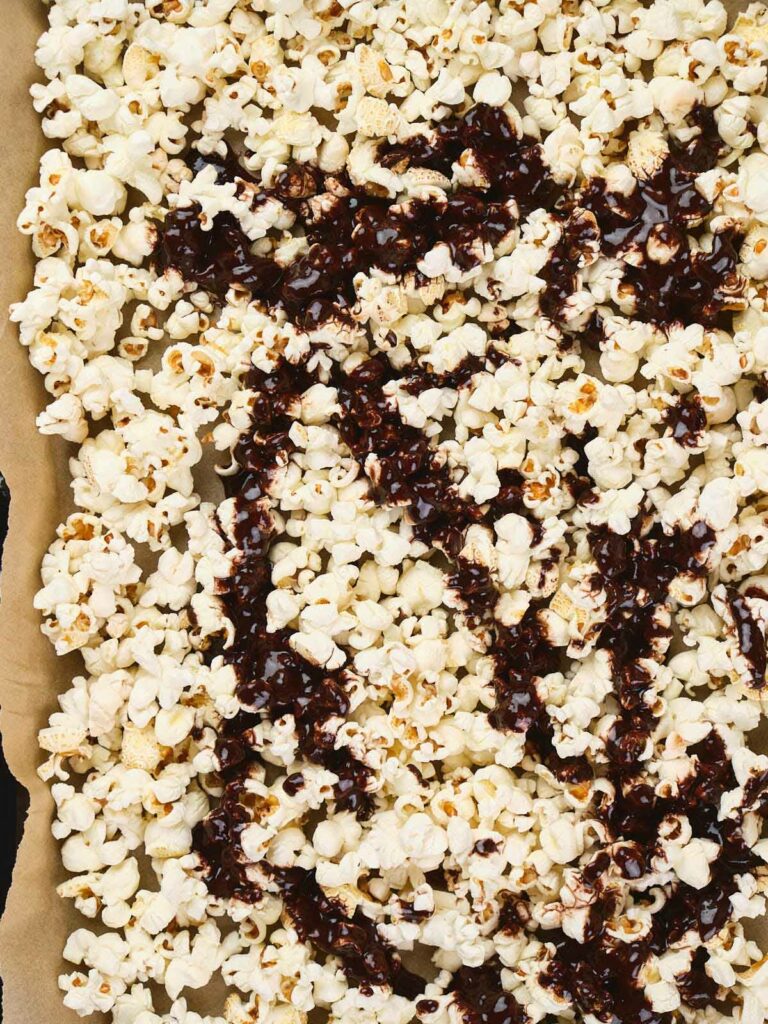 A baking tray filled with popcorn is drizzled with melted chocolate.