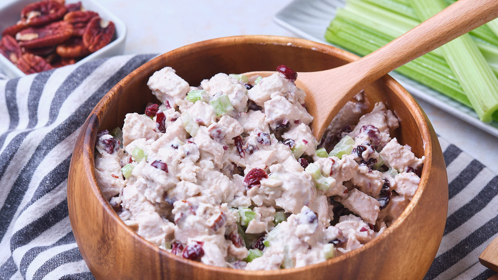 A wooden bowl filled with cranberry chicken salad with a wooden spoon.