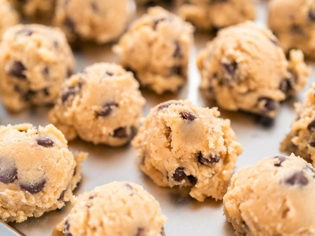 Close-up of raw chocolate chip cookie dough balls placed on a baking tray, ready to be baked.