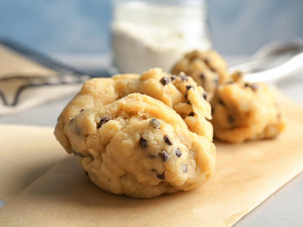 Close-up of raw cookie dough with chocolate chips on a piece of parchment paper.