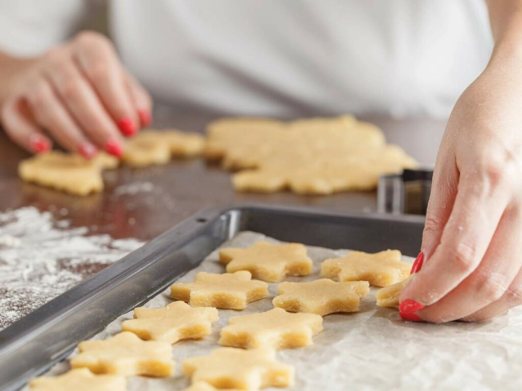 Person with red nail polish placing star-shaped dough pieces on a baking sheet lined with parchment paper.