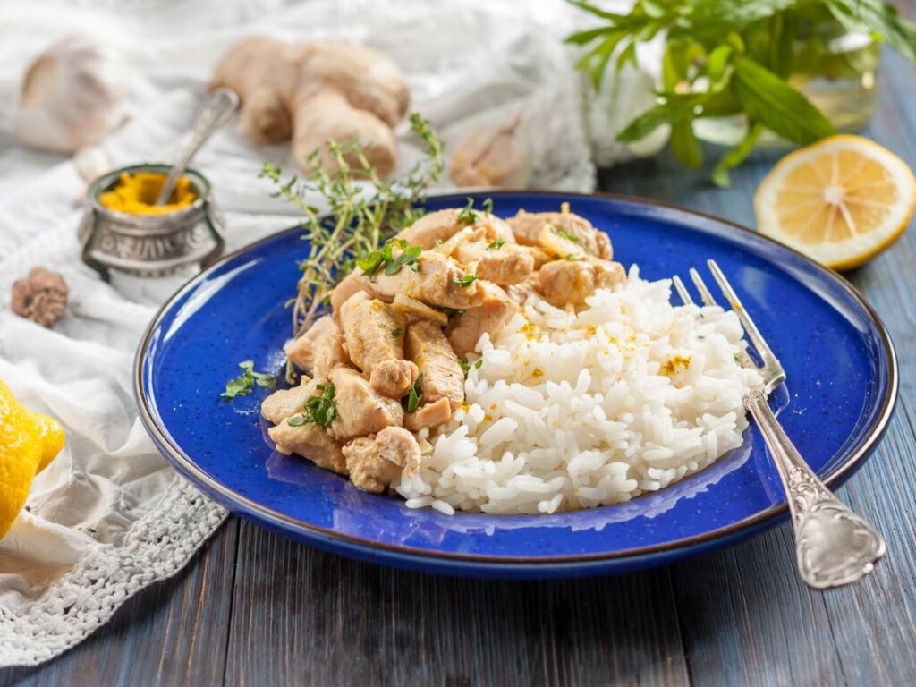 A blue plate with cooked white rice and sliced chicken garnished.