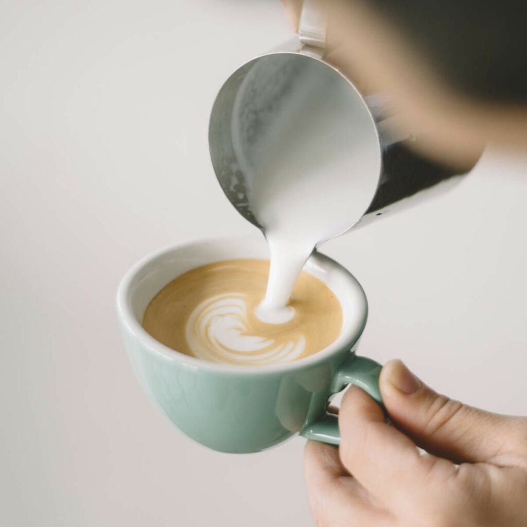 A person pours steamed milk into a cup of coffee.