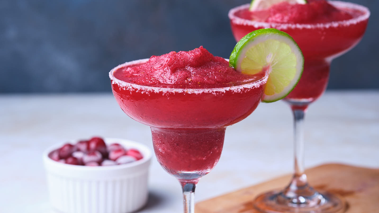 Two red frozen cranberry margaritas garnished with lime slices.