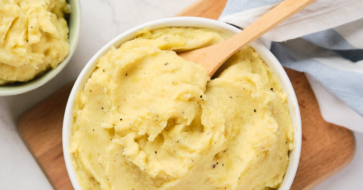 A bowl of garlic mashed potatoes with a wooden spoon, placed on a wooden board.